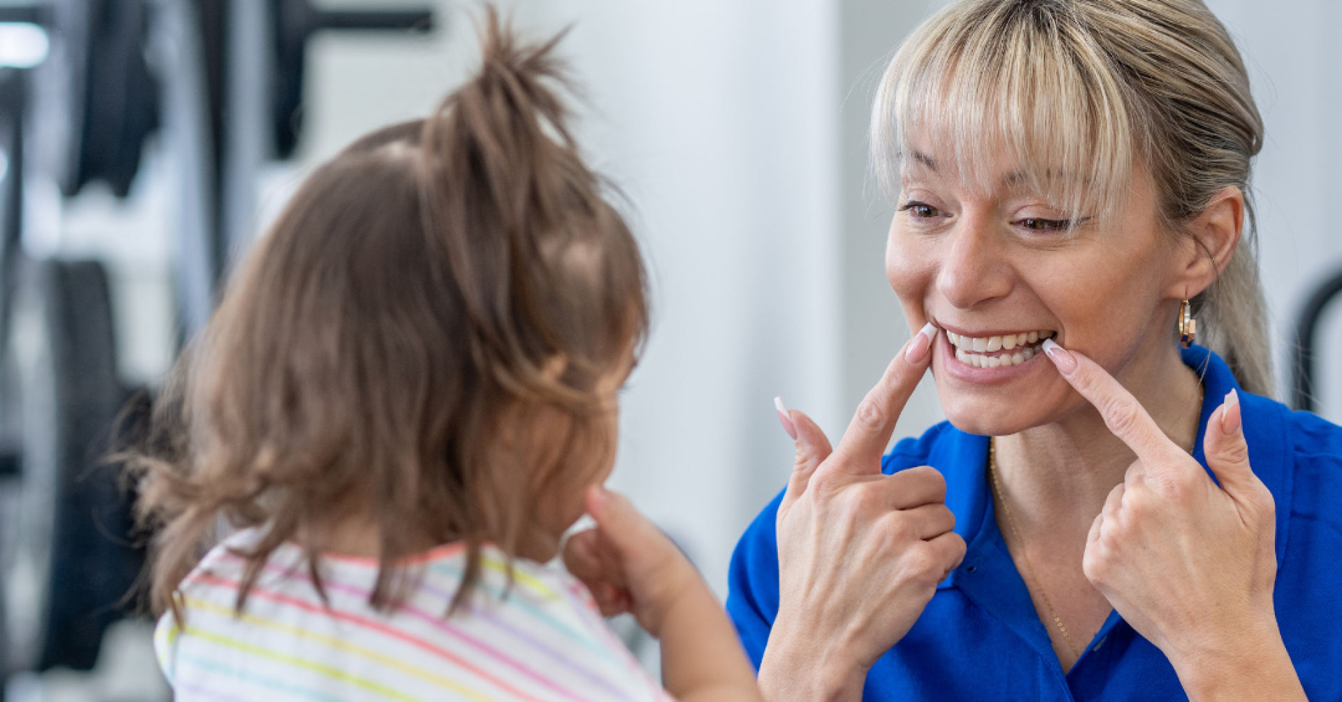 Physiotherapeutin zeigt einem kleinen Mädchen Sprachübungen