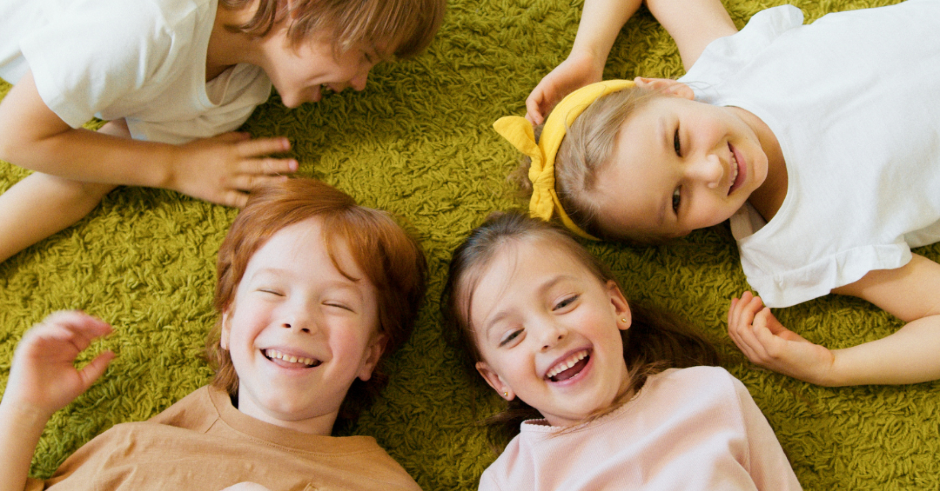 Fröhliche Kinder spielend auf grünem Teppich Lachende Kinder liegen auf grünem Teppich