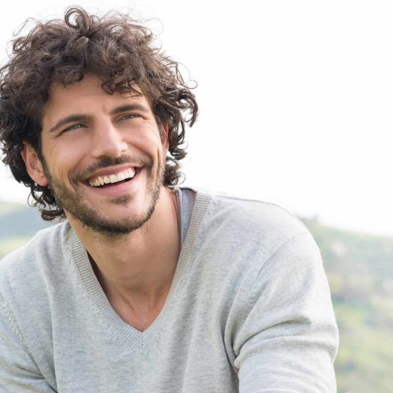 Lachender Mann mit Locken in der Natur Porträt eines lachenden Mannes im Freien mit lockigem Haar in grauem Pullover