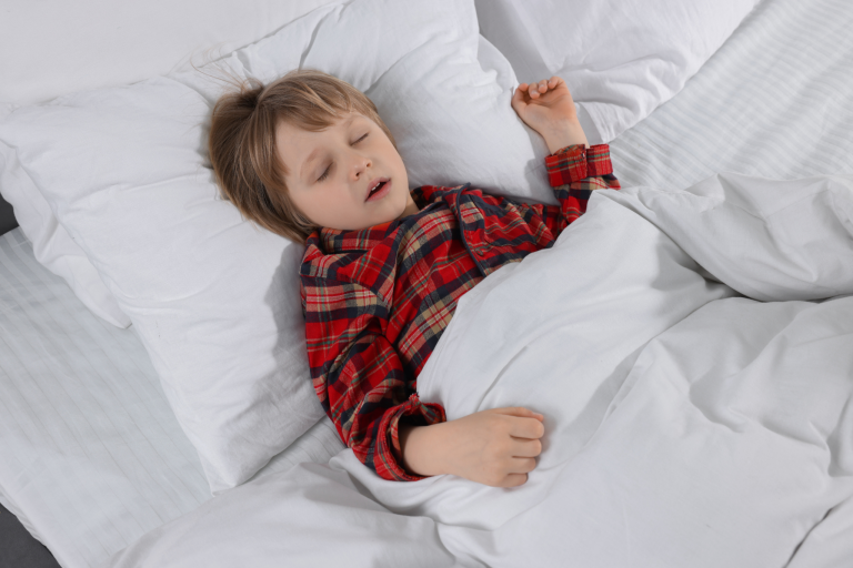 Kind schläft in einem Bett mit rotem Karohemd und weißen Kissen